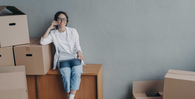 woman-sitting-on-the-phone-with-moving-boxes-surrounding-her