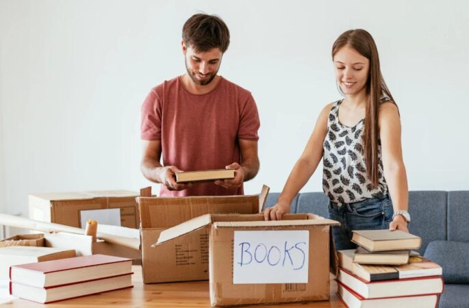 A couple packing books into boxes at home, preparing for a move or self storage – exploring how much self storage costs in the UK.